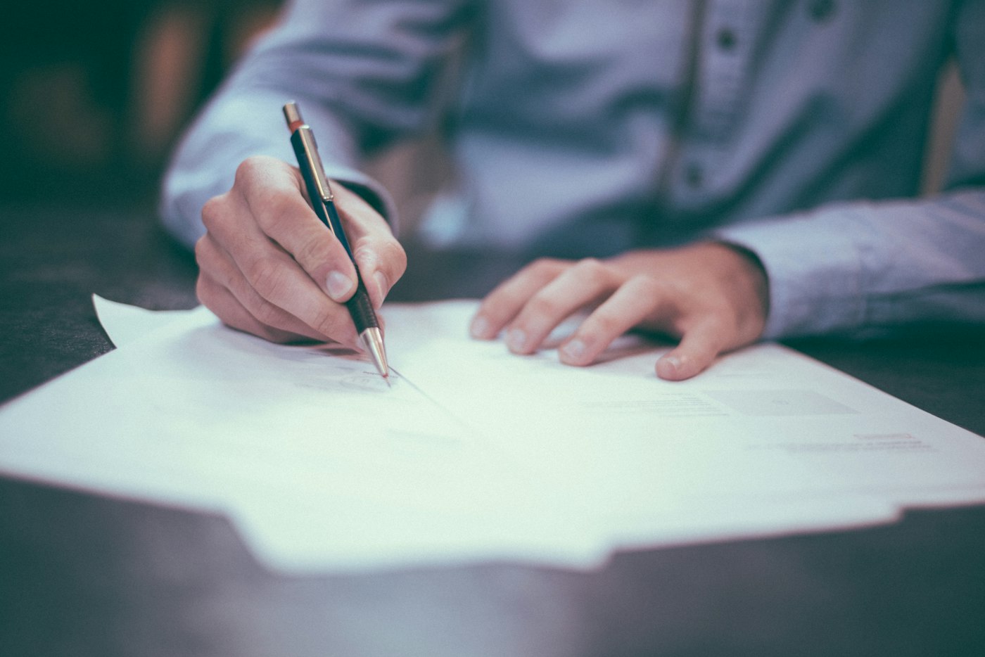 Persona firmando documentos sobre un escritorio